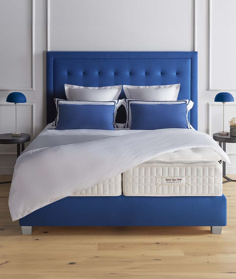Blue upholstered bed with white bedding and a mattress with Treca Rivoli topper in a room setting.