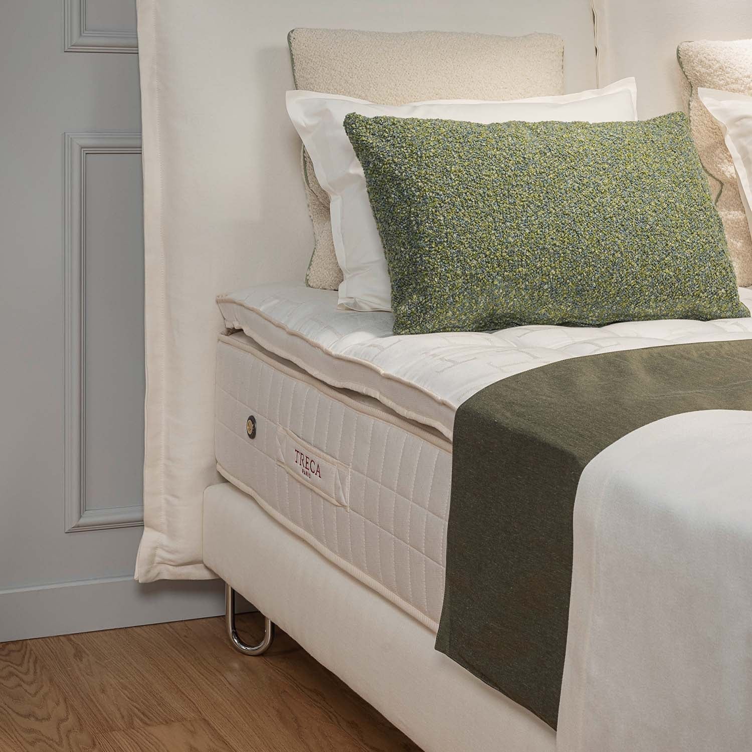 Bed with treca omega spring bed base and green decorative pillow against a gray wall.