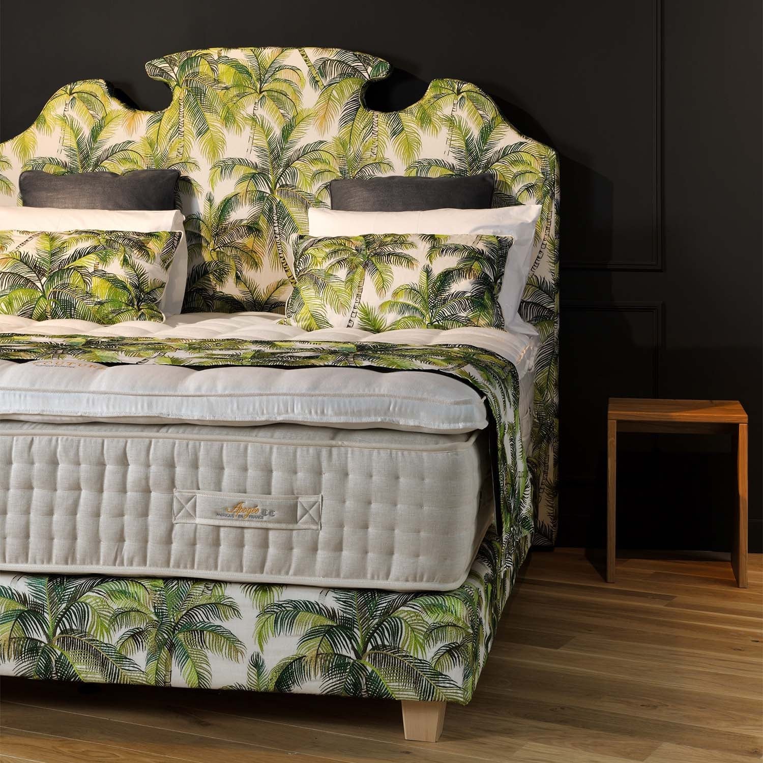 Bed with palm tree patterned headboard anda Treca grand confort bed base in a room with a wooden floor and dark walls.