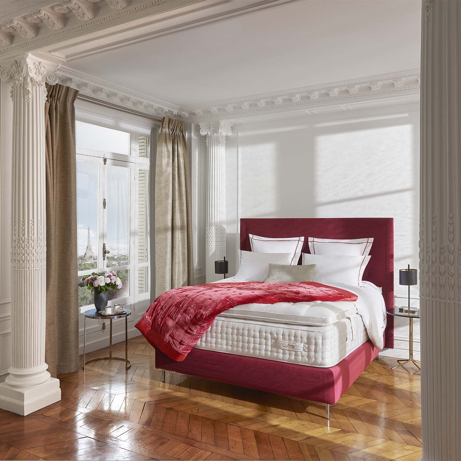 Red bed with white bedding on a mattress with a Treca Couture topper in a stylish bedroom with large windows.