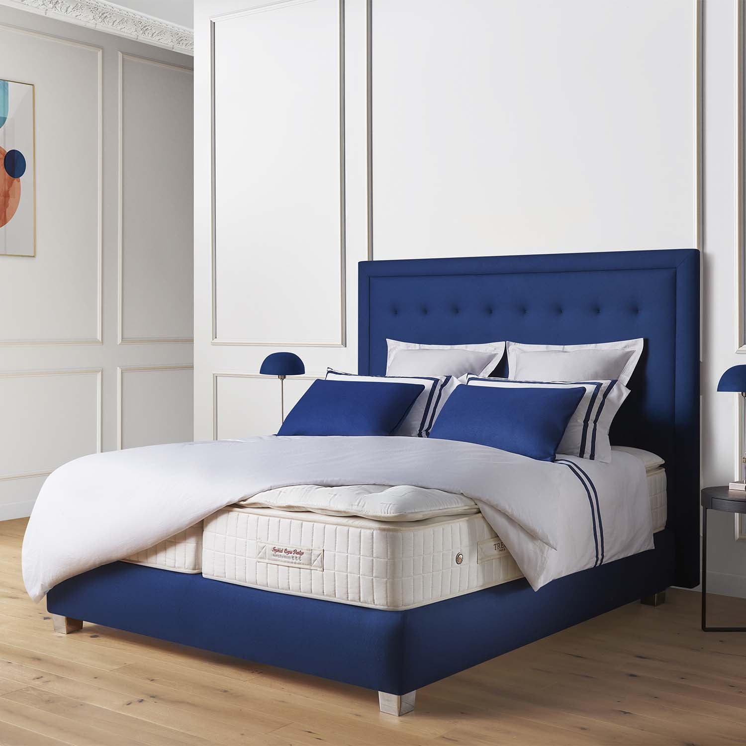 Bedroom with a bed featuring a blue headboard and white bedding on a mattress with Treca Rivoli topper